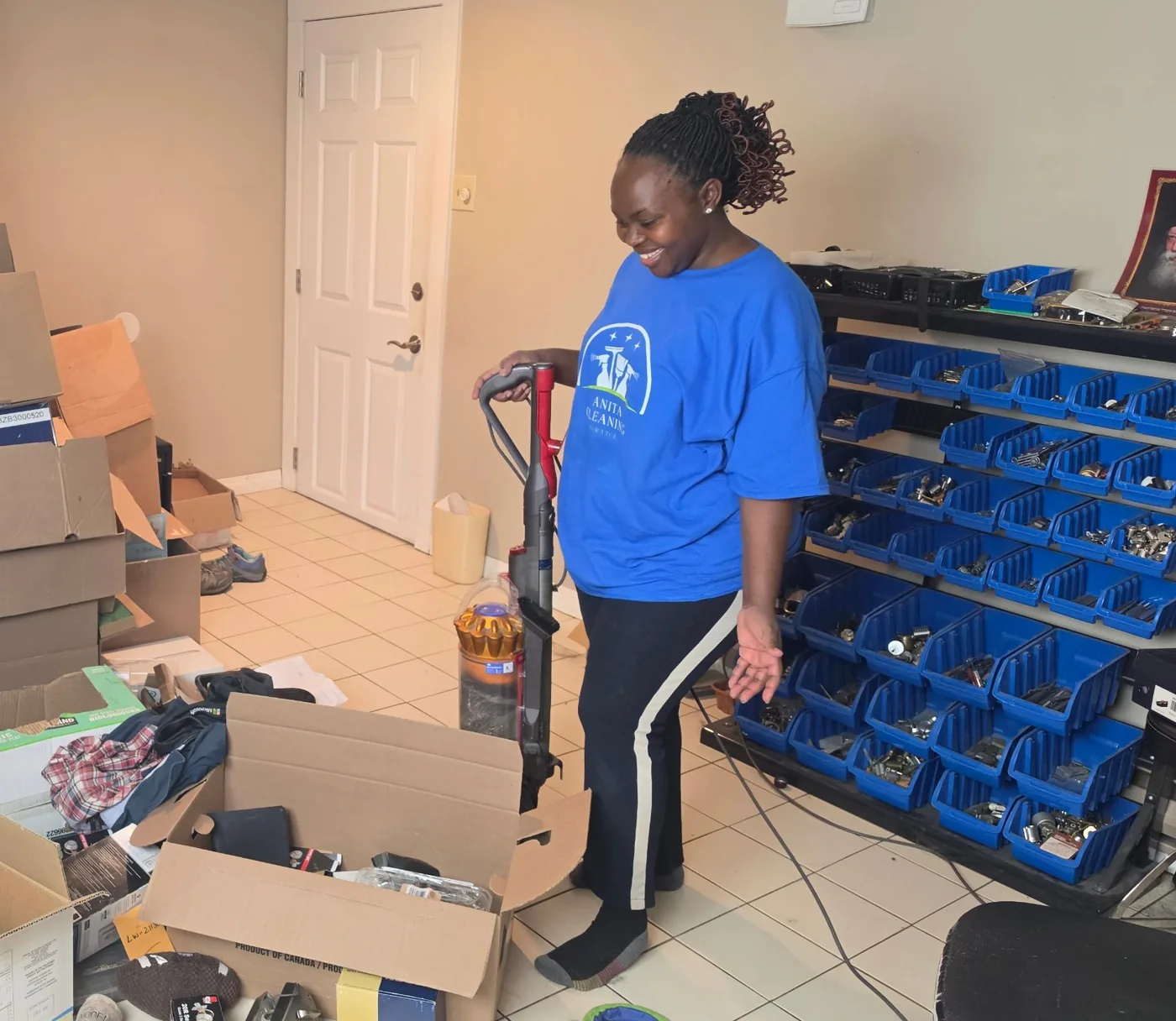 Anita, smiling, vacuum in hand, in her Anita Cleaning Service shirt